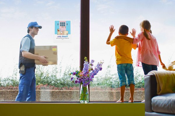 man delivering package to a house with children in house looking out to him